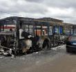A man drives past a public transport bus which was burned during a protest